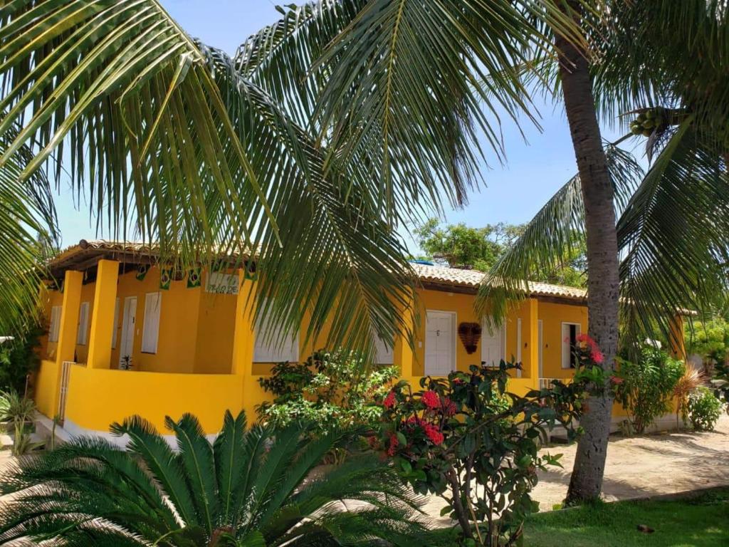 una casa amarilla con palmeras delante en Pousada Grão de Areia Beira Mar, en Mangue Seco