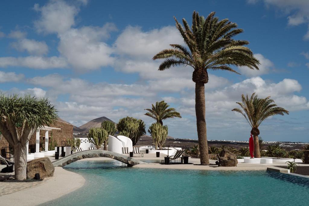 a swimming pool with palm trees and a bridge at Hotel Cesar Lanzarote in La Asomada