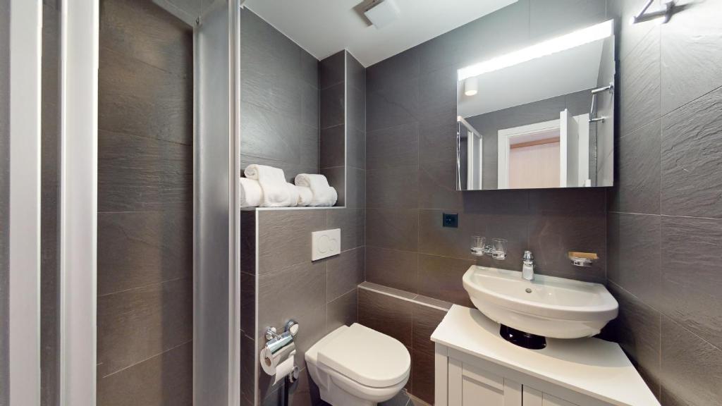 ein Badezimmer mit einem WC, einem Waschbecken und einem Spiegel in der Unterkunft Le Belvedere By Alaia in Crans-Montana