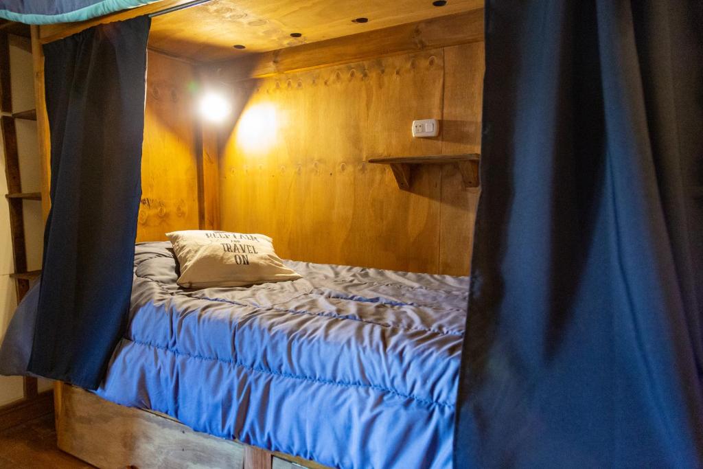 Cama en habitación con cortina azul en Hostel Cosmo en El Bolsón
