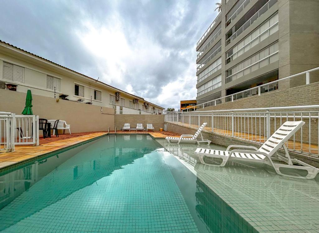 a swimming pool with lounge chairs and a building at Apto a 350m da Praia de Maitinga em Bertioga SP in Bertioga