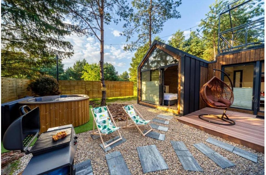 een kleine achtertuin met een zwart huis en stoelen bij Domki Marzeń w Marzyszu , Jacuzzi & Sauna in Marzysz