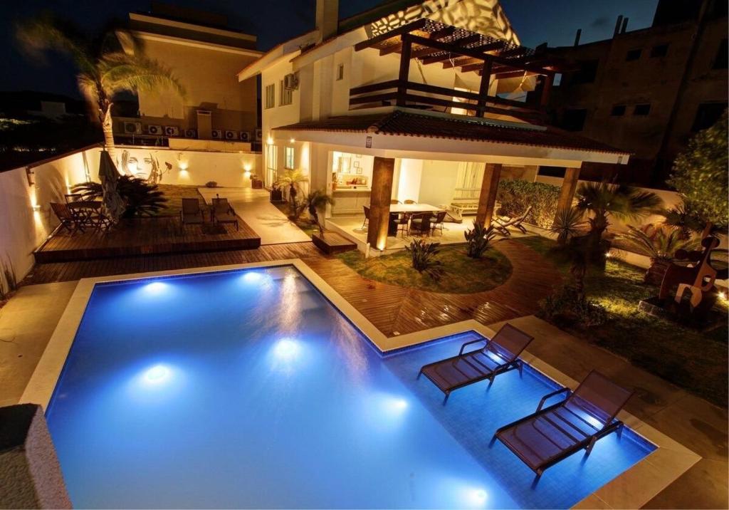 a swimming pool with chairs and a house at night at Casa do Artista a 60m do mar, piscina, 4 quartos in Bombinhas