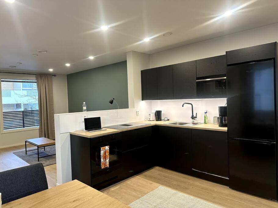 uma cozinha com armários pretos e um frigorífico preto em Kotimaailma Apartments#4 - Moderni, tilava kaksio keskustassa em Seinäjoki