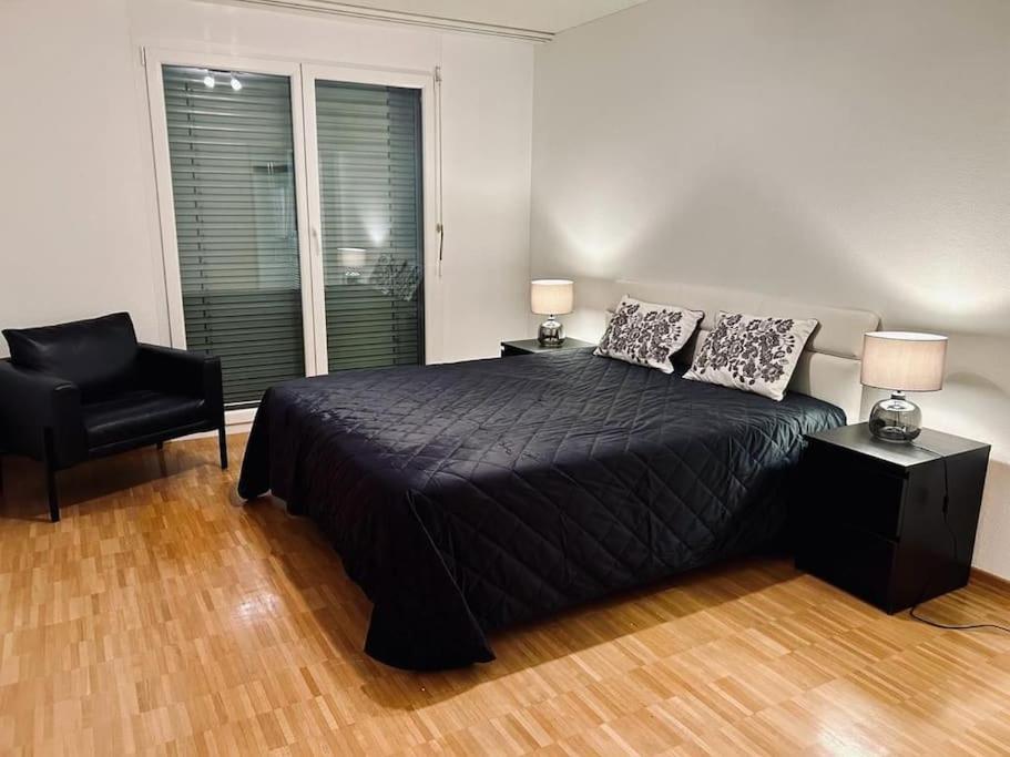 een slaapkamer met een zwart bed en een stoel bij Schöne 3.5 Zimmer-Wohnung mit Wintergarten in Fällanden