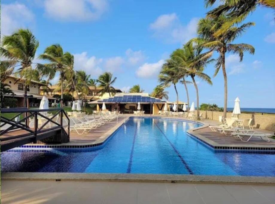 una piscina en el complejo con sillas y palmeras en Itacimirim Villas da Praia en Camassari