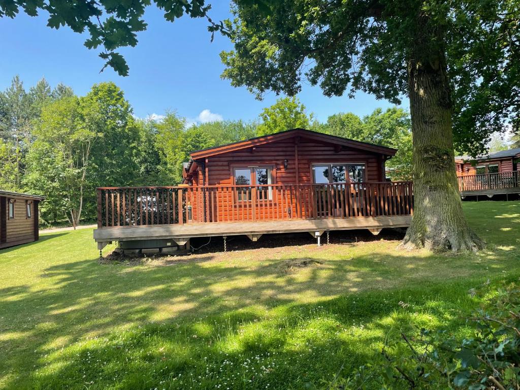 a log cabin with a large deck next to a tree at The Fairways, Kenwick Retreats in Louth