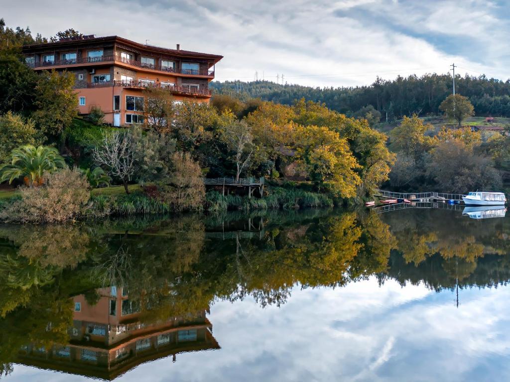 una casa en una colina junto a un río con árboles en Hotel Rural Quinta da Conchada en Aguieira
