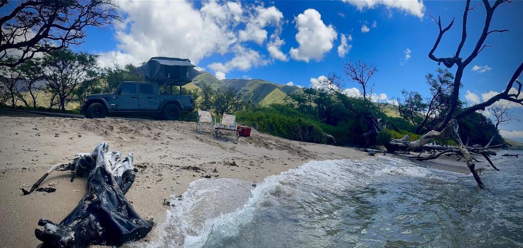 a blue truck parked on a sandy beach at Embark on a journey through Maui with Aloha Glamp's jeep and rooftop tent allows you to discover diverse campgrounds, unveiling the island's beauty from unique perspectives each day in Paia