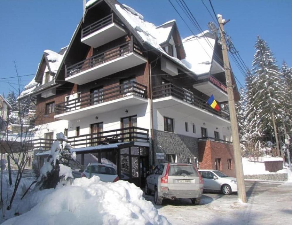 a snow covered building with cars parked in front of it at Aparthotel La Manastire in Sinaia