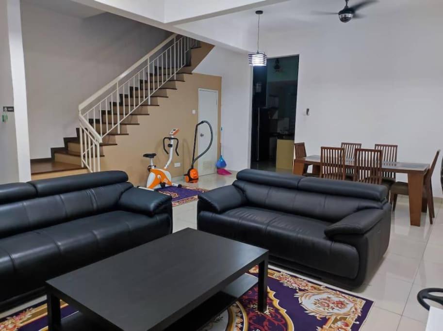 a living room with black leather furniture and a staircase at Layyin's Damai Residences in Shah Alam
