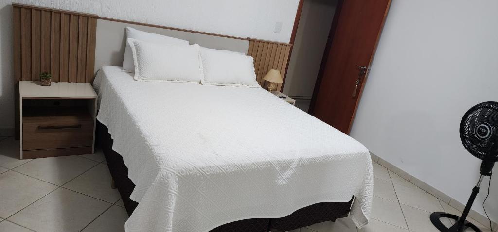 a bedroom with a large white bed with a fan at Quartos no Apartamento Neves in Araxá