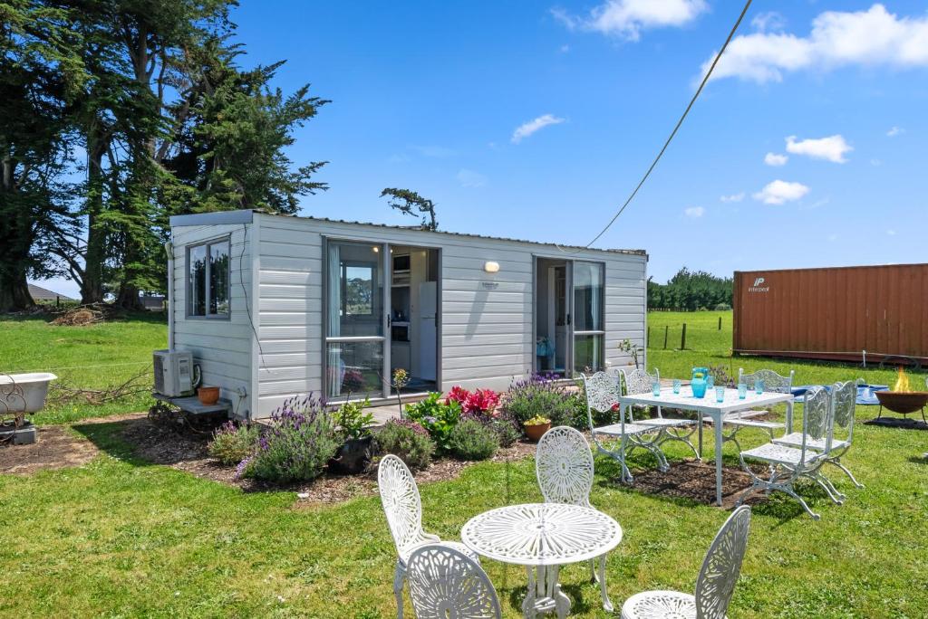 a tiny caravan in a yard with chairs and a table at MGM Studio Cabin - Himitangi Holiday Studio in Foxton