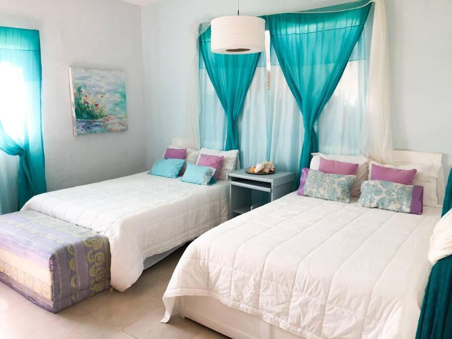 Duas camas num quarto com cortinas azuis e cor-de-rosa em Hermosa Casa en Chelem A 5 min Caminando de Playa em Chelem