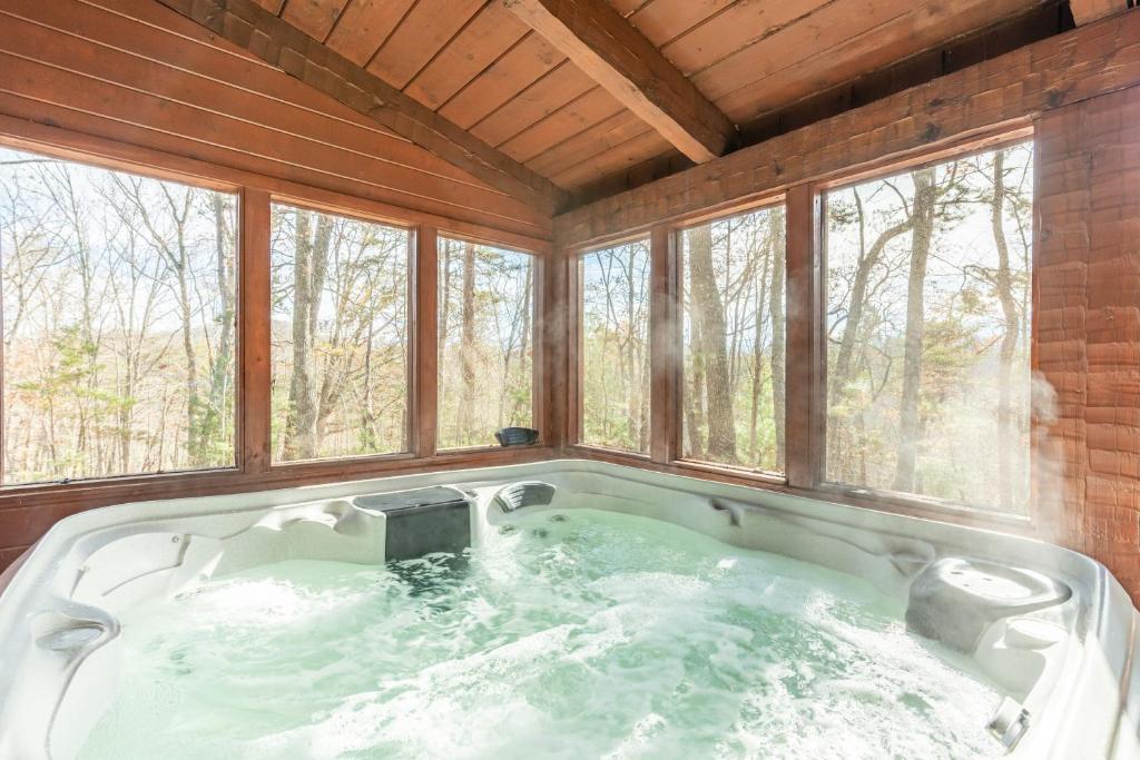 a large bath tub in a room with windows at Dudley II by AvantStay Comfortable Cabin w Hot Tub Views in Pigeon Forge