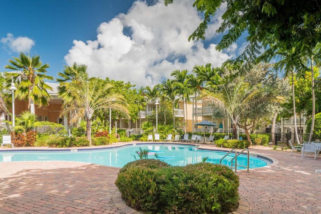 a swimming pool with palm trees in front of a building at Coral Palm by AvantStay Key West Walkable Gated Community Shared Pool Month Long Stays Only in Stock Island