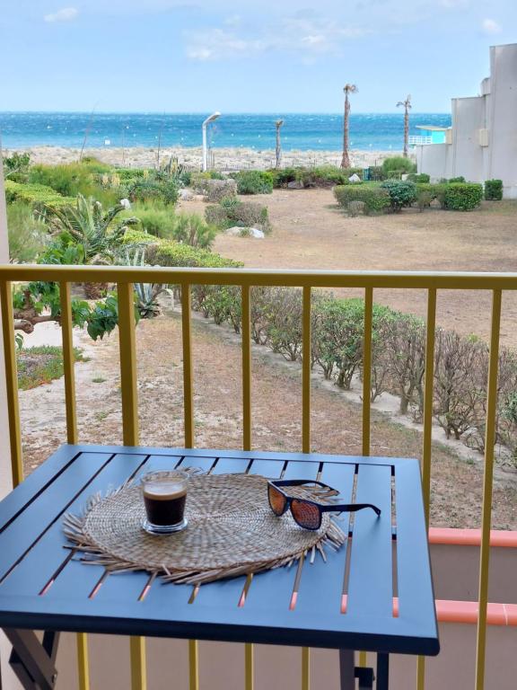a table with sunglasses and a cup of coffee on a balcony at Magnifique studio cosy vu mer avec Wifi in Le Barcarès