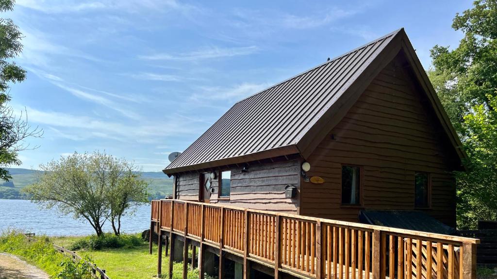 a cabin with a wooden deck next to a body of water at Lochside Lodge in Dallavich