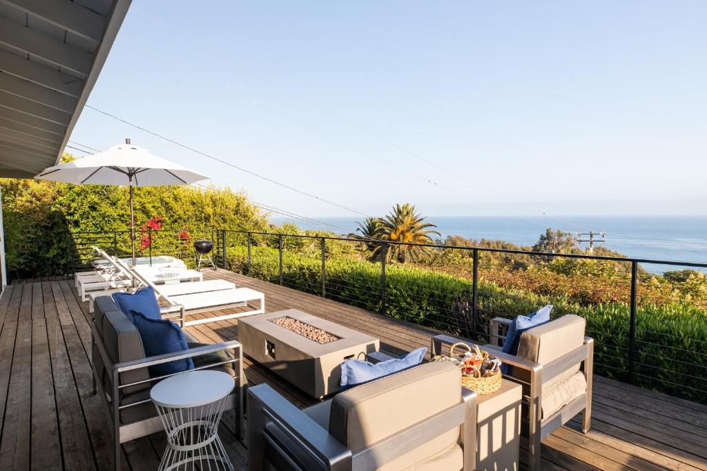 a deck with chairs and an umbrella and the ocean at Bluff by AvantStay Gorgeous Malibu Getaway w Hot Tub Spectacular Ocean Views in Malibu
