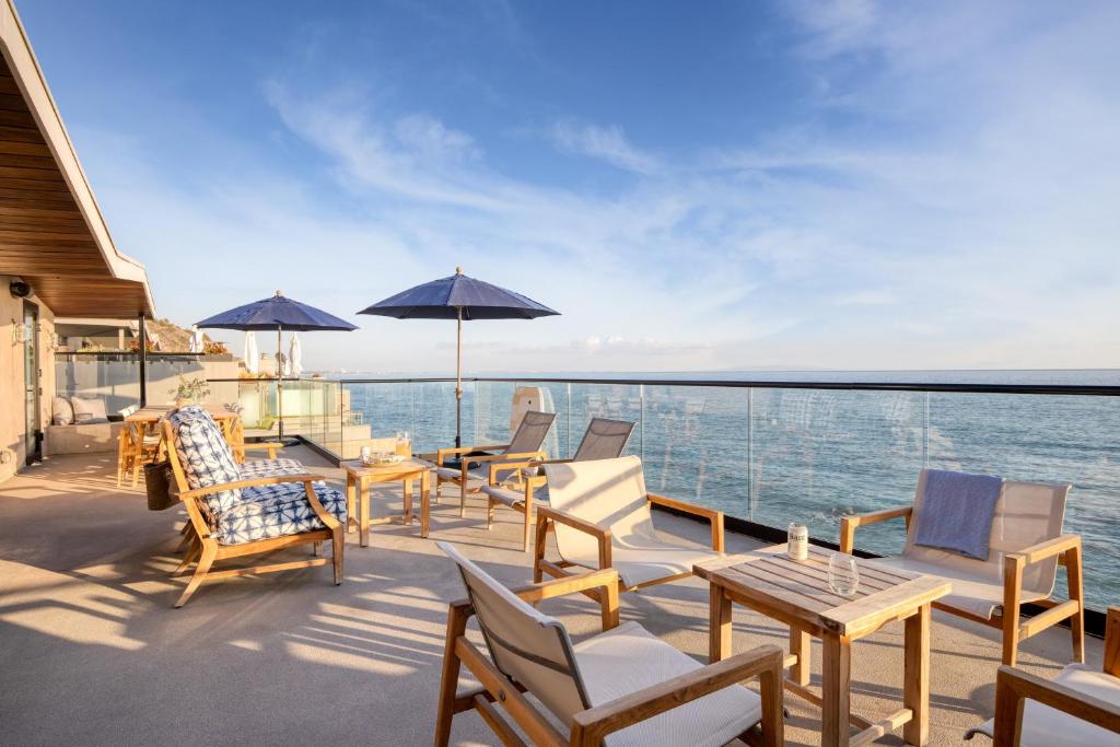 a deck with chairs tables and umbrellas on the water at Matador by AvantStay Ocean Front Malibu Pad w Rooftop Patio in Topanga