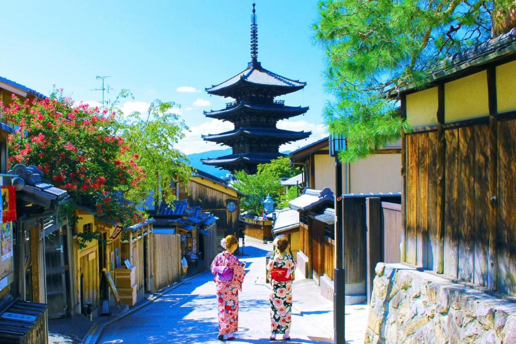 京都的住宿－純和風料理旅館Kinoe，两个和服上的女人在一条带有宝塔的街道上走着