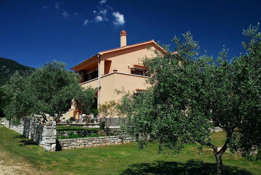 a house with a stone wall and trees in front of it at House ALEXANDRA in Nerezine in a quiet location on Losinj island in Nerezine