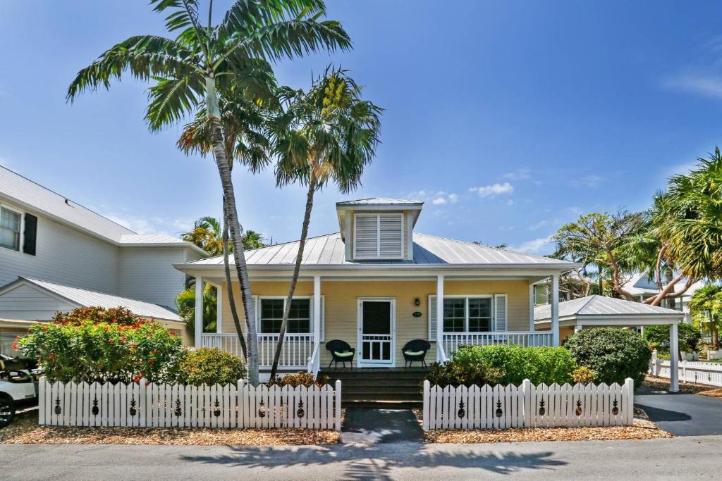 une maison jaune avec une clôture blanche et des palmiers dans l'établissement Spa Oasis by AvantStay Shared Pool 3 Miles to Smathers Beach Month Long Stays Only, à Stock Island