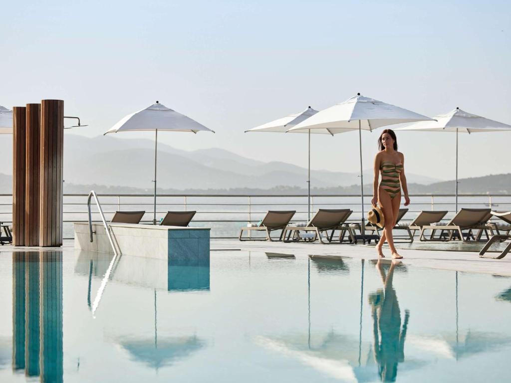 a woman walking next to a swimming pool at Sofitel Golfe d'Ajaccio Thalassa Sea & Spa in Ajaccio