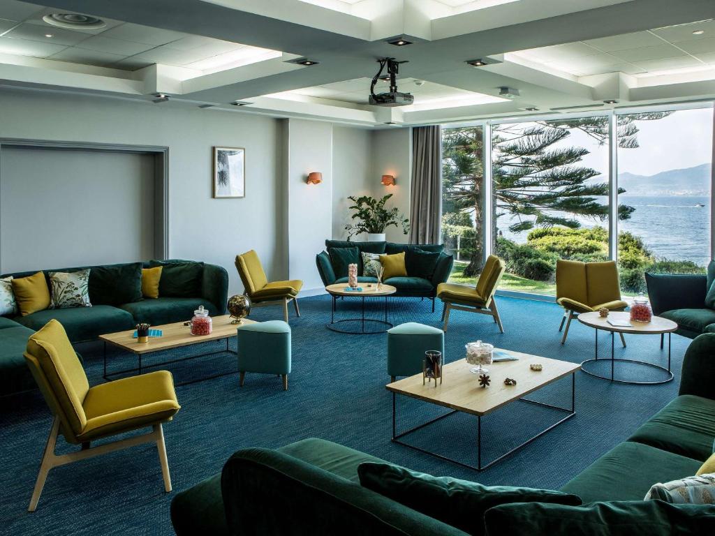 a living room with couches and tables and windows at Sofitel Golfe d'Ajaccio Thalassa Sea & Spa in Ajaccio