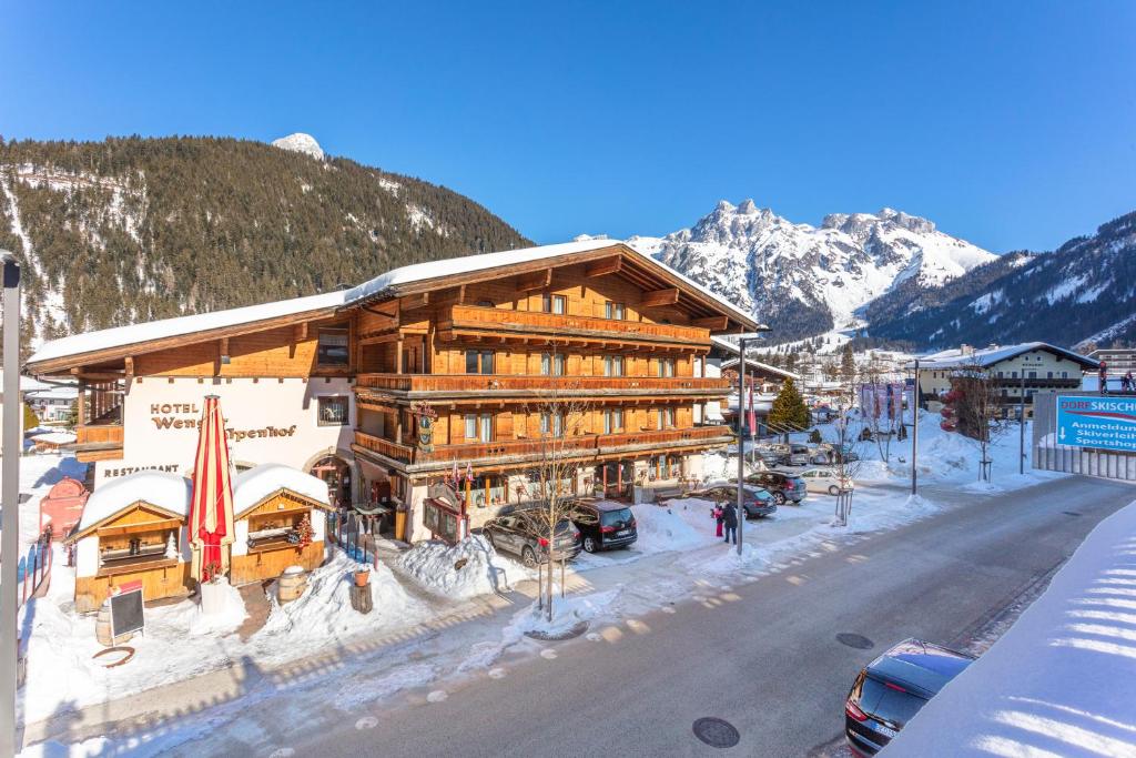 a large wooden building with a snow covered mountain at Hotel Wenger Alpenhof in Werfenweng