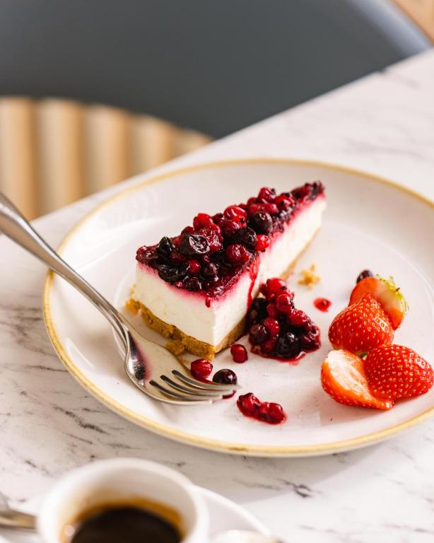a piece of cake with berries on a plate with a fork at Leonardo Inn Aberdeen Airport in Dyce
