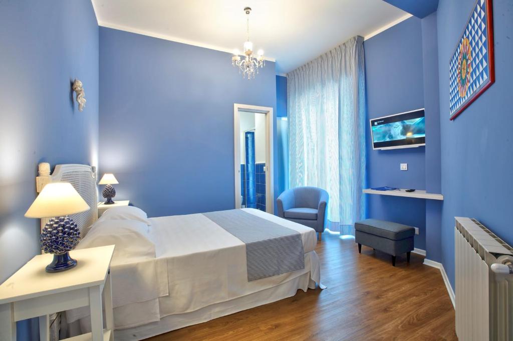 ein blaues Schlafzimmer mit einem Bett, einem Tisch und einem Stuhl in der Unterkunft B&B Del Corso in Capo dʼOrlando