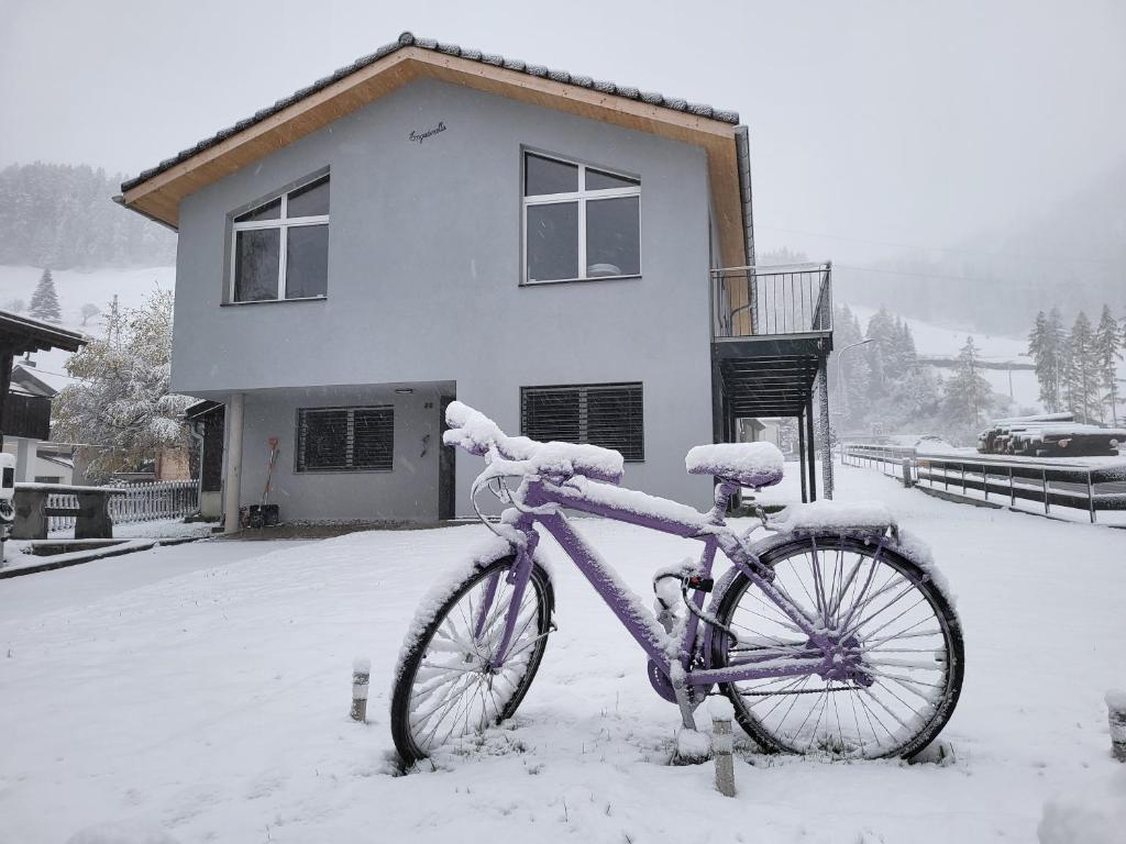 a bike parked in the snow in front of a house at Splügen Haus Engadinella in Splügen