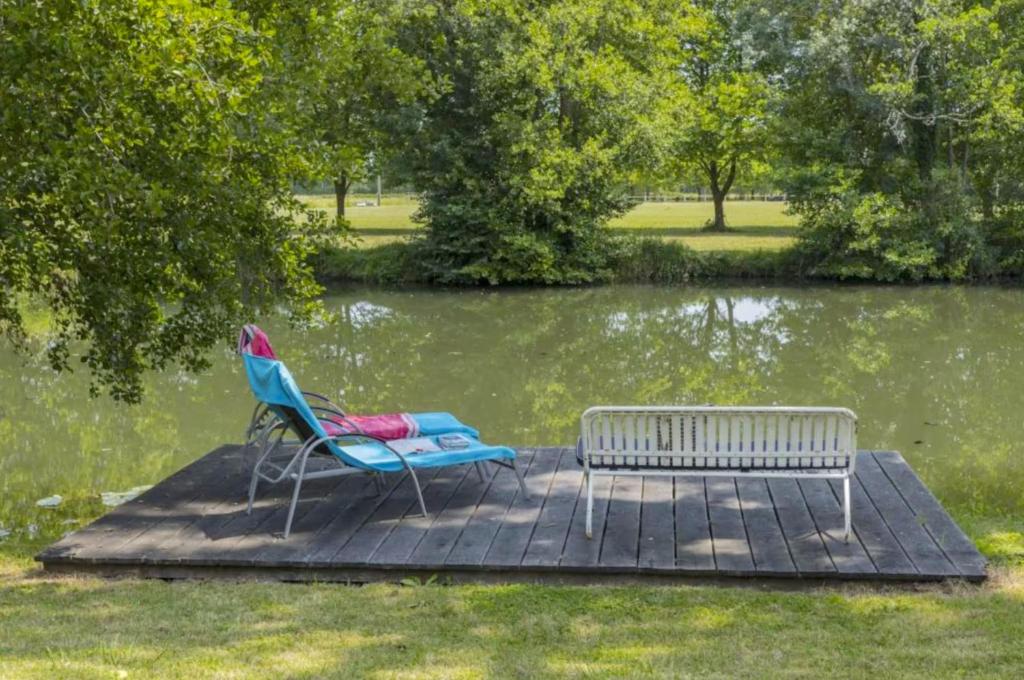 un banco y una silla en un muelle junto a un lago en Au bord de la Dronne, en Bonnes