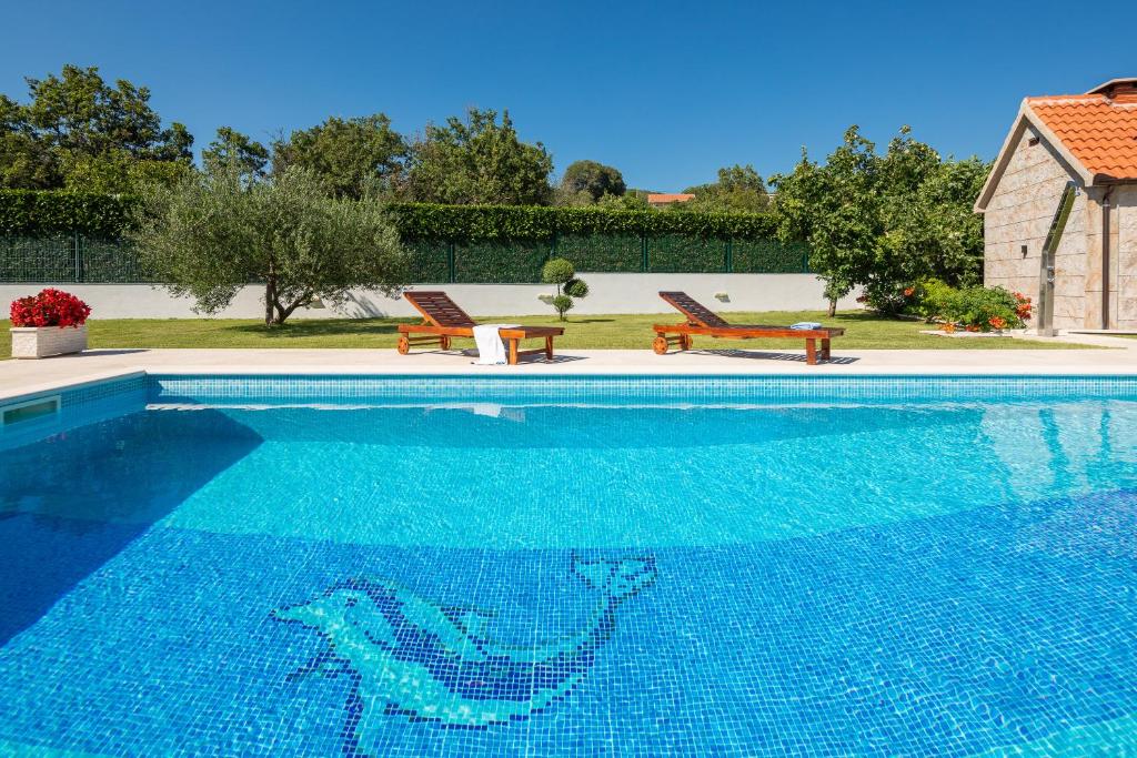 a large blue swimming pool with two chairs and a house at Villa Paradiso in Blato na Cetini