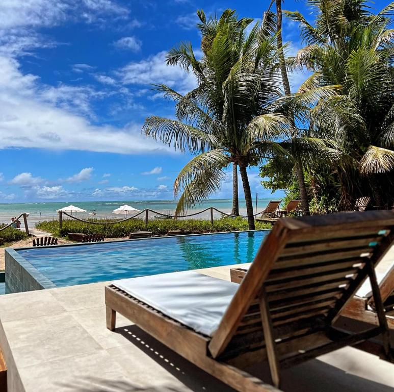 a pool with a chair and palm trees and the ocean at Pousada Casotas in Pôrto de Pedras