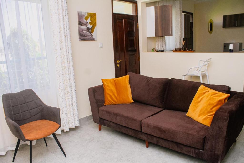 a living room with a brown couch and a chair at Twin Palms Apartments, Bamburi, Mombasa in Mombasa