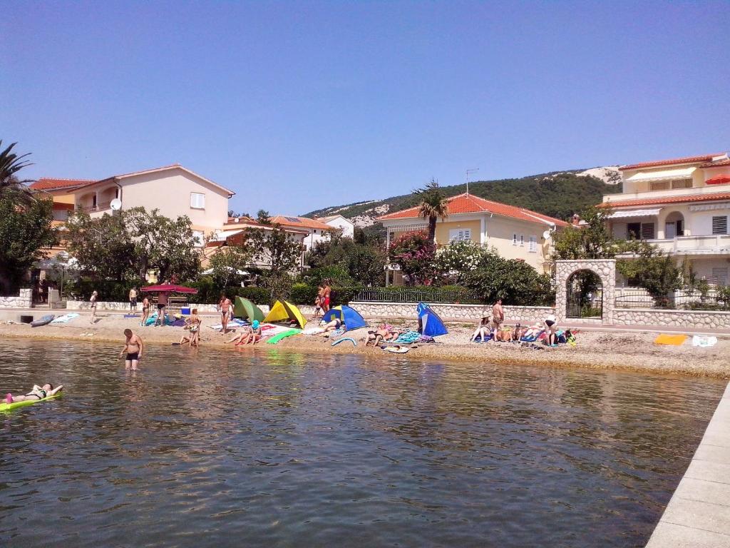a group of people sitting on the beach near the water at Apartments Antica in Rab