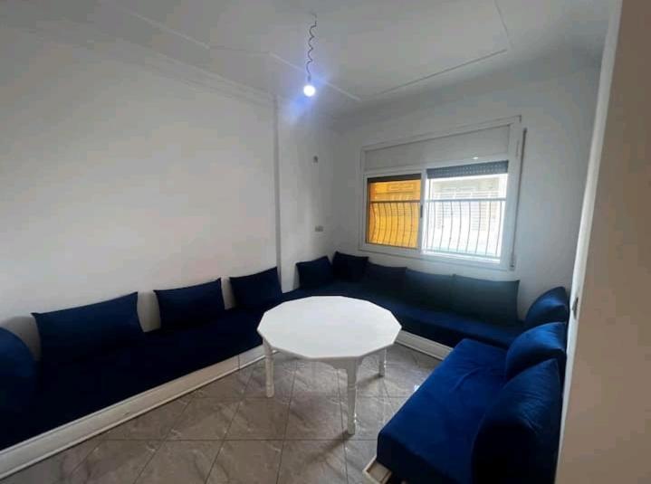 uma sala de estar com um sofá azul e uma mesa em Nouvel appartement idéal em Guercif