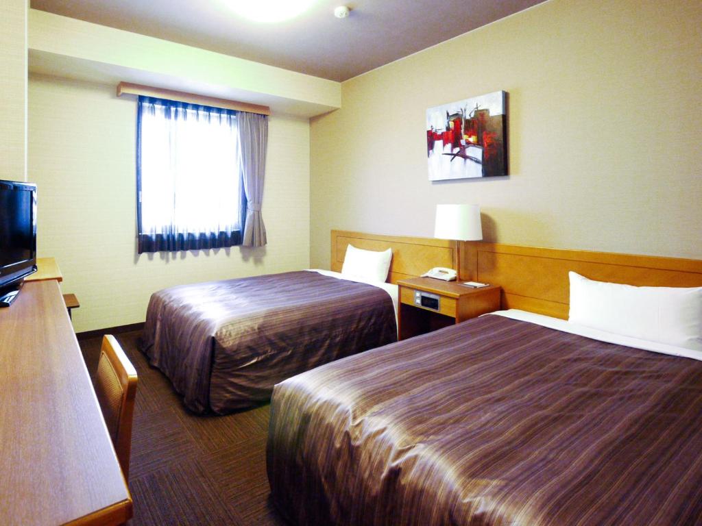 a hotel room with two beds and a television at Hotel Route-Inn Tajimi Inter in Tajimi