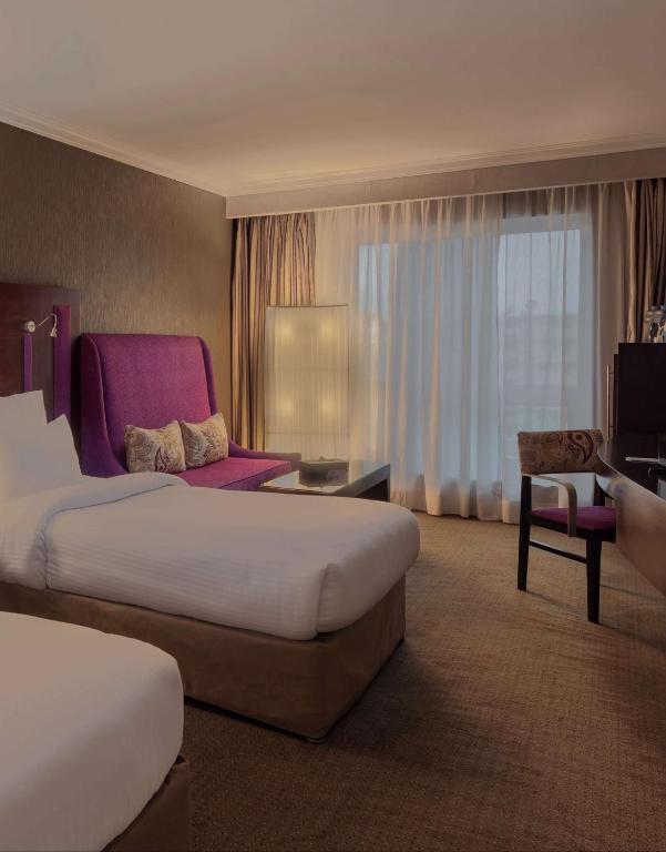 a hotel room with two beds and a chair at Radisson Blu Hotel, Cairo Heliopolis in Cairo