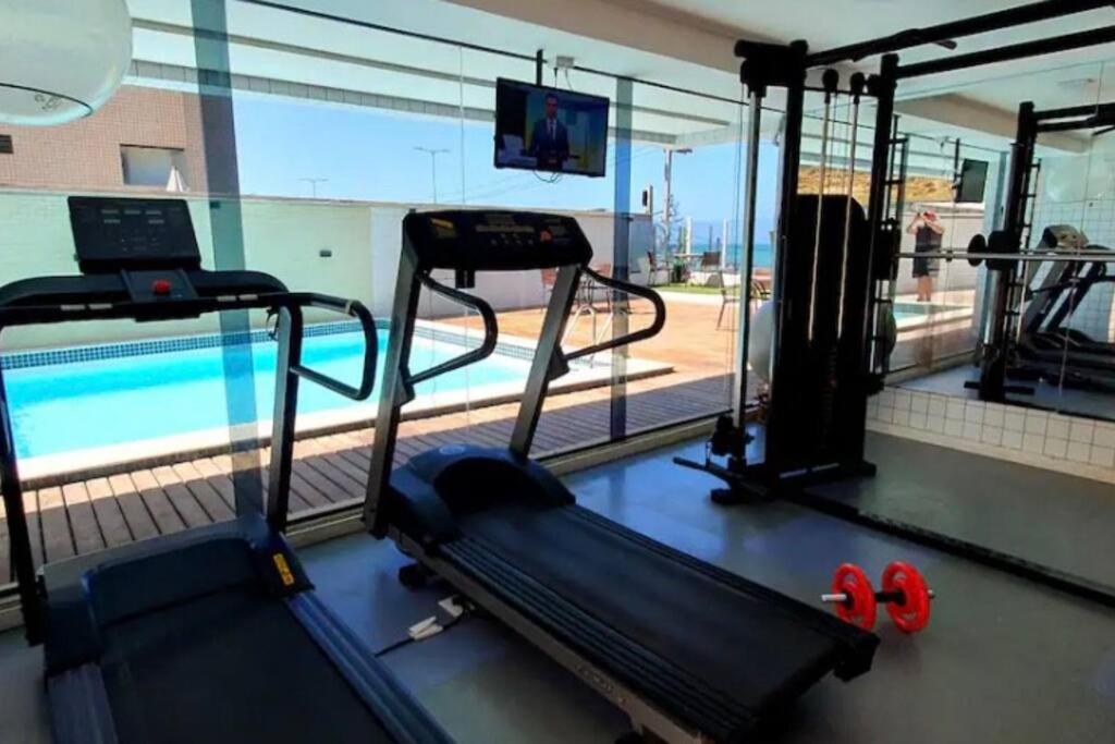 a gym with a treadmill and a swimming pool at Flat Alto Padrão Beira Mar in Natal