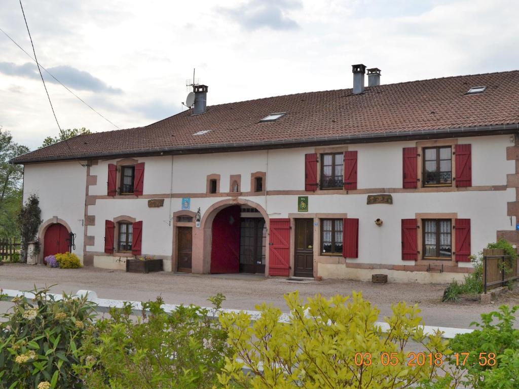 - un grand bâtiment blanc avec des portes et des fenêtres rouges dans l'établissement Gîte spacieux avec terrasse, 3 chambres, équipements bébé, à 16 km de Gérardmer - FR-1-589-23, à Aumontzey