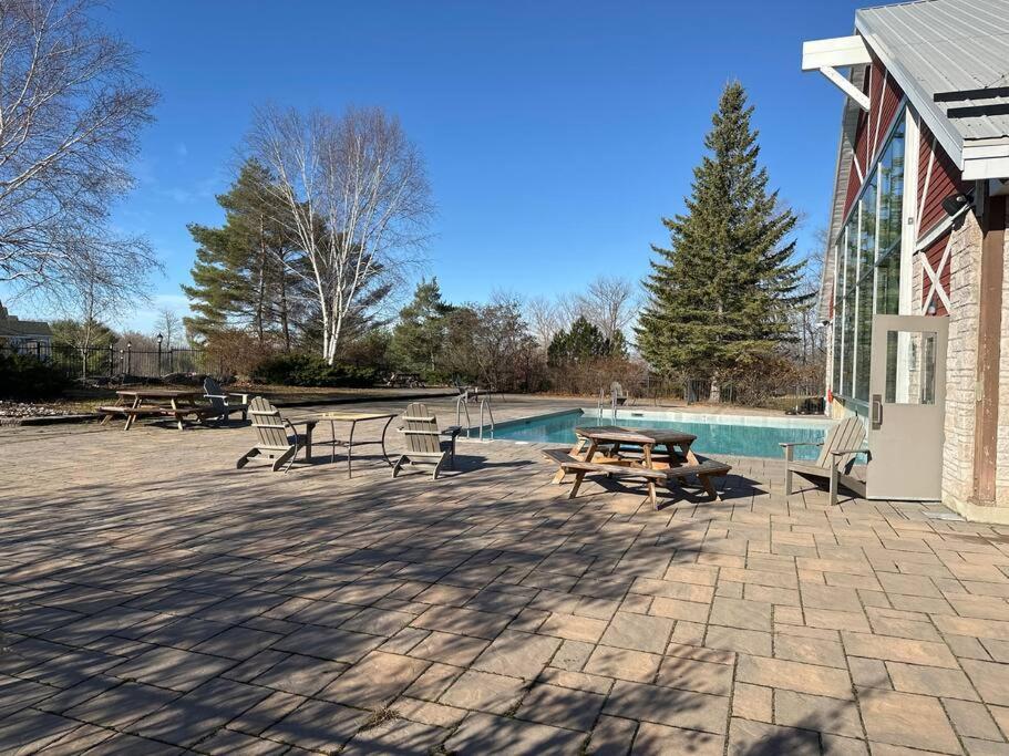 un patio con mesas y bancos junto a una piscina en Relax & Rejuvenate at 2BR Retreat with Pool & Gym en Shanty Bay