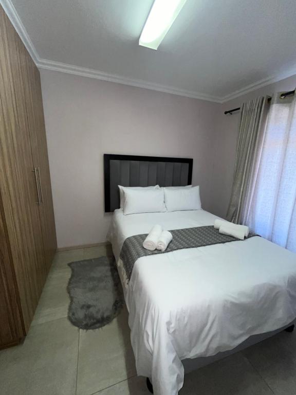 um quarto com uma cama grande e lençóis brancos em Vigne Palm Inn apartment em Gqeberha