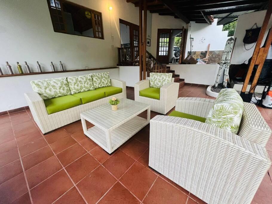 sala de estar con mesa y muebles de mimbre blanco en Rincón del colibrí/casa campestre/piscina/la vega, en La Vega