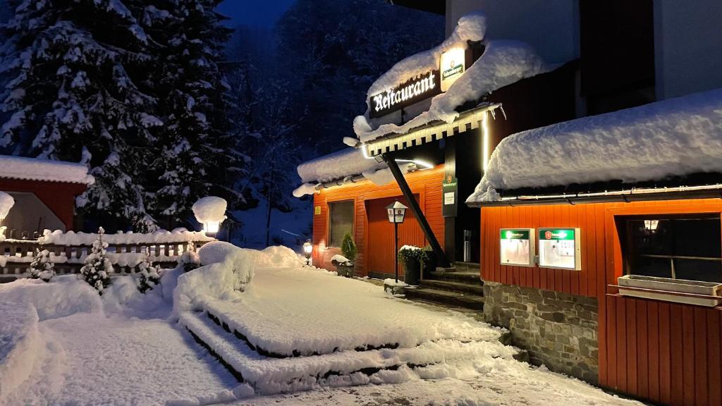 une maison recouverte de neige devant un bâtiment dans l'établissement Gasthof Paluda - Pizzeria, à Dalaas