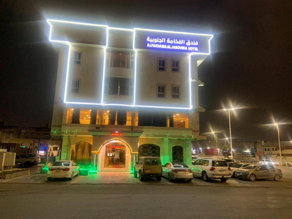 un edificio con coches estacionados en un estacionamiento por la noche en الفخامة الجنوبية للشقق المخدومة en Jazán