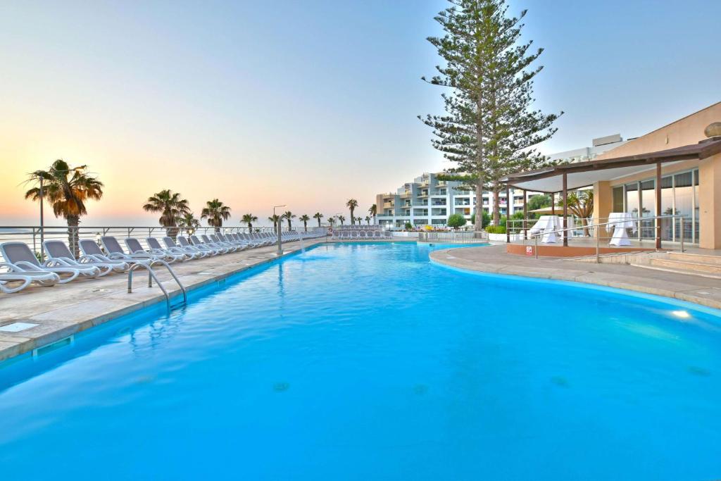 a large swimming pool with chairs and a resort at DoubleTree by Hilton Malta in St Paul's Bay