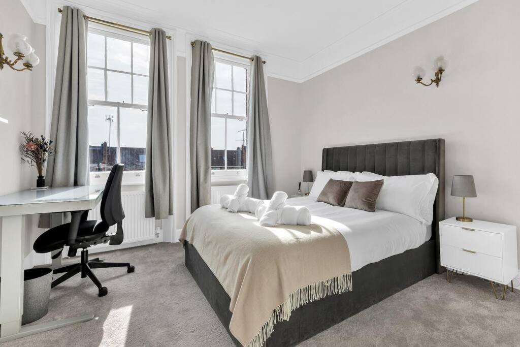 a white bedroom with a bed and a desk and windows at Luxury 3 bedroom apartment in the heart of High Street Kensington, London. in London